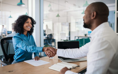 Smiling African American manager sitting at his desk in an office shaking hands with a job applicant after an interview