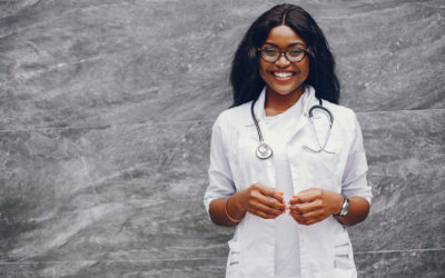 Stylish black doctor in a white uniform. Lady with stethoscope. Woman standing near gray wall
