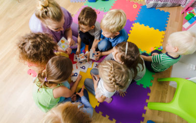 Group of kindergarten kids sitting closely on a floor together with teacher, providing group work. Children learning to cooperate while solving tasks.